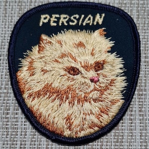 May include: A black and white embroidered patch with a fluffy, orange Persian cat. The patch has the word "PERSIAN" in white letters on a black background.