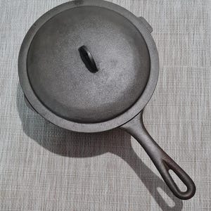 May include: A black cast iron skillet with a lid. The skillet has a long handle with a loop at the end. The lid has a small handle on top.