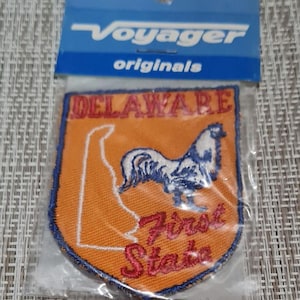 May include: An orange embroidered patch with a blue outline. The patch features a white rooster with a blue tail and the text "DELAWARE First State".