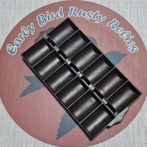 May include: A dark brown cast iron mold with 12 rectangular compartments. The mold is on a red and brown circular background with the text "Early Bird Rusty Relics".