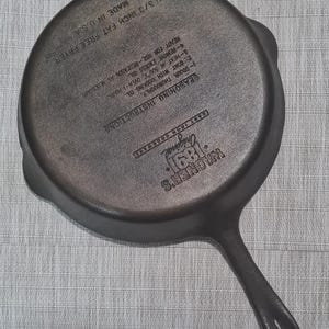 May include: A black cast iron skillet with a long handle. The skillet is 11 3/3 inches in diameter and is made in the USA. The text "WAGNER'S Original 1891 CAST IRON COOKWARE" is printed on the skillet. The text "SEASONING INSTRUCTIONS" is printed on the skillet, followed by a list of instructions for seasoning the skillet.