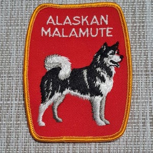 May include: Red embroidered patch with a yellow border featuring a black and white Alaskan Malamute dog and the text "Alaskan Malamute".
