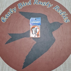 May include: A small, packaged sticker featuring a black and white graphic of a squirrel. The sticker is on a brown and orange background with the text "Voyager originals". The background is a brown circle with a bird silhouette and the text "Early Bird Rusty Relics".