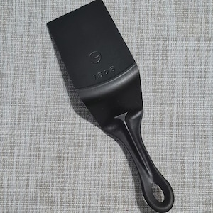 May include: A black metal spatula with a long handle and a rounded tip. The spatula has the number "9" and "1503" embossed on the blade.