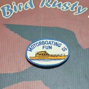May include: Oval patch with the text "MOTORBOATING IS FUN" and an illustration of a yellow boat. The patch has a white background with a blue border. The patch is on a brown and maroon background.