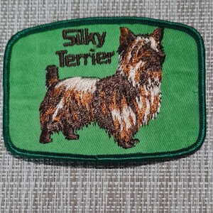 May include: Green embroidered patch with a brown and white Silky Terrier dog and the text "Silky Terrier".