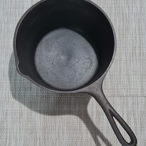 May include: A black cast iron skillet with a single handle. The skillet is empty and has a smooth, dark surface.