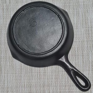 May include: Black cast iron skillet with a loop handle. The skillet has a smooth, black surface and a raised number "3" on the bottom.