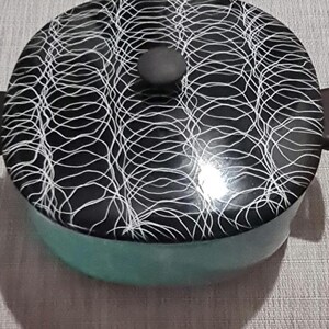 May include: A black and white patterned ceramic pot with a teal blue interior and a black knob on the lid.