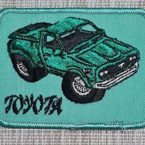 May include: A green embroidered patch with a green Toyota pickup truck and the word "TOYOTA" in black lettering.