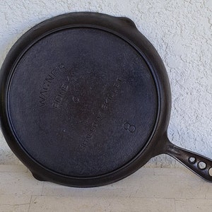 May include: Black cast iron Wagner Sidney, Ohio shallow skillet with the text "SHALLOW SKILLET" and the number "8" on the bottom.