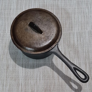 May include: A cast iron pot with a lid and a handle. The pot is dark brown and has a rustic look.