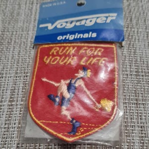May include: Red embroidered patch with a yellow border. The patch features a cartoon figure running with a yellow object in their hand. The text "RUN FOR YOUR LIFE" is written in yellow letters on the patch.