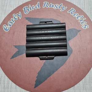 May include: A cast iron Tiny Corn Stick pan, marked "No. 23-S", sits on a round, red and brown surface with a bird silhouette and the text "Early Bird Rusty Relics" in a blue, curved font. The pan has six parallel, rounded molds.