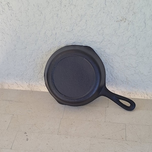 May include: A black cast iron skillet with a round cooking surface and a long handle.