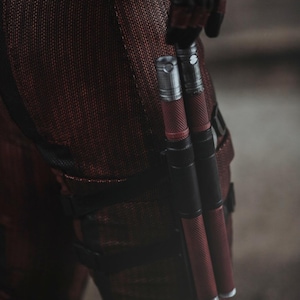 Könnte beinhalten: Nahaufnahme einer Person, die ein rot-schwarzes Kostüm trägt, mit zwei silbernen und schwarzen Metallstöcken, die an ihrem Bein befestigt sind.