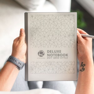 Puede incluir: Un lector electrónico blanco con un borde gris y un lápiz gris. La pantalla muestra un cuaderno de cuadrícula de puntos con el texto "Deluxe Notebook Dot Grid Style" y el logotipo "remarkable".