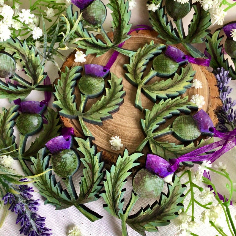 May include: A collection of wooden ornaments shaped like thistles, painted in shades of green and purple. The ornaments are decorated with intricate details and have a rustic charm.
