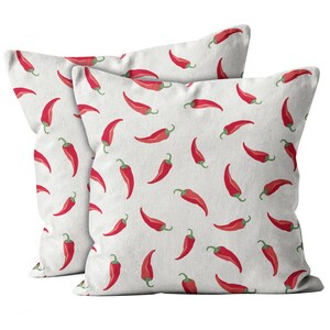 May include: Two square throw pillows with a white background and a repeating pattern of red chili peppers with green stems. The pillows are made of a soft fabric and are suitable for a living room or bedroom.