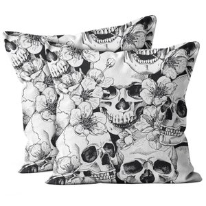 May include: Two decorative throw pillows with a black and white skull and floral design. The pillows feature a detailed illustration of skulls intertwined with blooming flowers, creating a gothic and botanical theme.