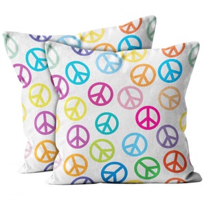 May include: Two white throw pillows with a repeating pattern of colorful peace symbols in shades of blue, green, yellow, orange, pink, and purple. The pillows are square and appear to be made of a soft fabric.
