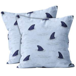 May include: Two light blue throw pillows with a repeating pattern of dark blue shark fins on a light blue background.