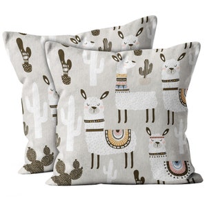 May include: Two beige pillowcases with a pattern of white llamas wearing colorful headbands and brown cacti. The llamas are surrounded by brown cactus plants.