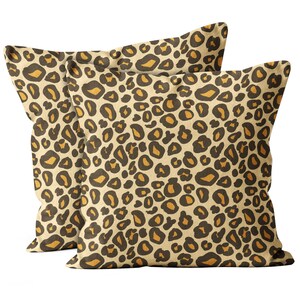 May include: Two square cushions with a leopard print design. The cushions have a beige background with brown and orange spots. The cushions are intended for decorative purposes.