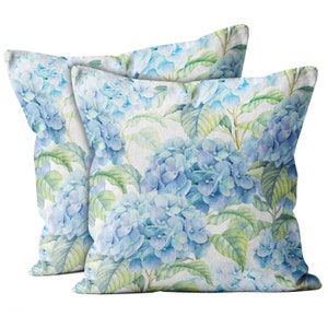 May include: Two decorative throw pillows with a watercolor floral pattern featuring blue hydrangeas on a white background.