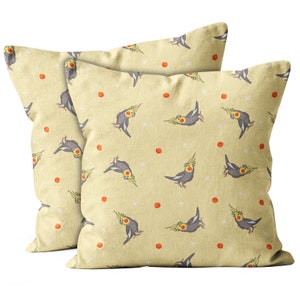 May include: Two yellow throw pillows with a repeating pattern of gray cockatiels and orange dots.