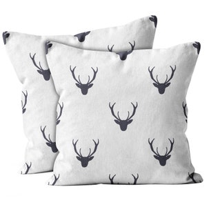 May include: Two white throw pillows with a repeating pattern of dark gray deer silhouettes. The pillows are made of a soft, textured fabric.