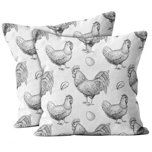 May include: Two square white cushions featuring a repeating monochrome pattern of chickens, eggs, and feathers. The design has a rustic, farmhouse style.