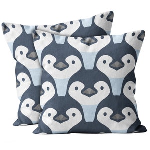 May include: Two square throw pillows with a repeating pattern of stylized penguins. The penguins are navy blue with white bellies, light blue accents, and gray beaks. The pillows are likely made of a soft fabric.