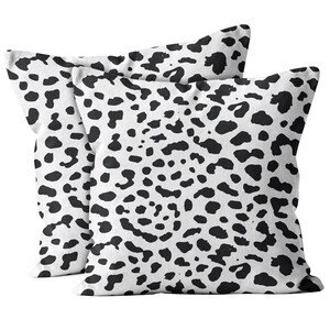 May include: Two square cushions featuring a white backdrop adorned with a black spotted design. The pattern resembles a Dalmatian's coat. These cushions are crafted from a soft material and are suitable for home decoration, adding a touch of style.