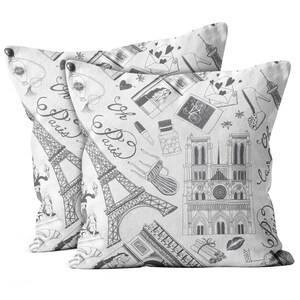 May include: Two white throw pillows with a black and gray Parisian theme. The design includes the Eiffel Tower, Notre Dame Cathedral, and the Arc de Triomphe. The pillows also feature sketches of perfume bottles, lipstick, and the words "Oh Paris".