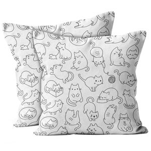 May include: Two white throw pillows with a repeating black line drawing pattern of playful cats in various poses. The cats are depicted with simple outlines, some interacting with toys or in boxes.