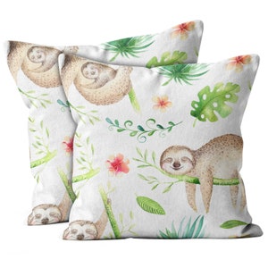 May include: Two white throw pillows with a watercolor pattern of sloths, tropical leaves, and flowers. The sloths are light brown and the leaves are green. The flowers are pink and orange.