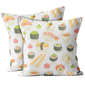 May include: Two white cushions featuring a repeating pattern of sushi, including nigiri, maki rolls, wasabi, ginger, and chopsticks. The sushi illustrations are in shades of orange, green, and brown.
