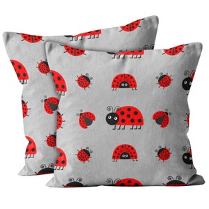 May include: Two gray pillowcases with a repeating pattern of red ladybugs with black spots and black legs. The ladybugs have black eyes and some are smiling.