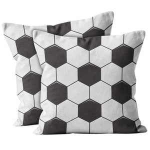 May include: Two square throw pillows with a soccer ball design. The pillows feature a pattern of black and white hexagons, mimicking the look of a soccer ball. The pillows are made of a soft fabric and are suitable for home decor.
