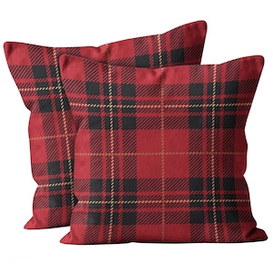 May include: Two square cushions featuring a red, black, and gold tartan pattern. The cushions are made from a soft material and are intended for decorative use on a sofa or bed. The tartan design is a traditional pattern.