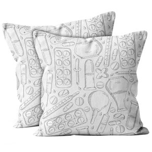May include: Two white throw pillows with a black and white doodle pattern of medical supplies, including pills, syringes, thermometers, and test tubes.