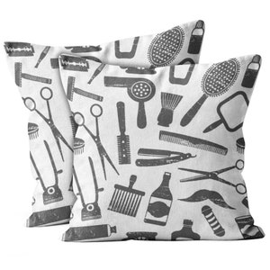 May include: Two white throw pillows with a repeating pattern of barber tools in gray. The pattern includes scissors, razors, hairbrushes, hair dryers, and bottles. The pillows are a decorative item for a barber shop or salon.