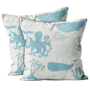 May include: Two square cushions with a nautical theme. The cushions are off-white with a light blue pattern of whales, octopuses, anchors, palm trees, and ship wheels. The cushions are made of a soft fabric.