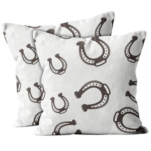 May include: Two white pillow covers with a brown horseshoe pattern. The pillow covers are made of a soft, textured fabric.