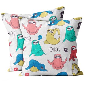 May include: Two white throw pillows with a repeating pattern of colorful sloths in yoga poses. The sloths are in shades of pink, blue, yellow, and green. The word "OM!" is written in black, along with speech bubbles.