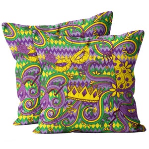 May include: Two purple, green, and yellow throw pillows with a Mardi Gras theme. The pillows feature a repeating pattern of crowns, masks, and party hats.