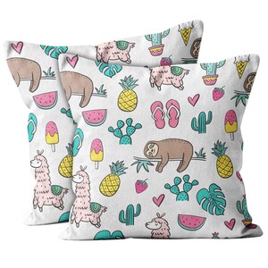 May include: Two white throw pillows with a repeating pattern of sloths, llamas, pineapples, cacti, watermelon slices, ice cream bars, flip-flops, hearts, and tropical leaves. The pillows are square and likely made of a soft fabric.