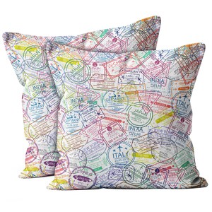 May include: Two square throw pillows with a repeating pattern of colorful travel stamps. The stamps include text and dates from various countries, such as Japan, India, and Italy. The pillows are white with a soft texture.