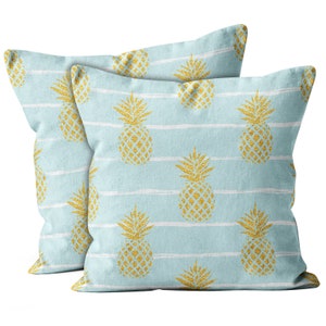 May include: Two light blue throw pillows with a white stripe pattern and gold glitter pineapple designs.